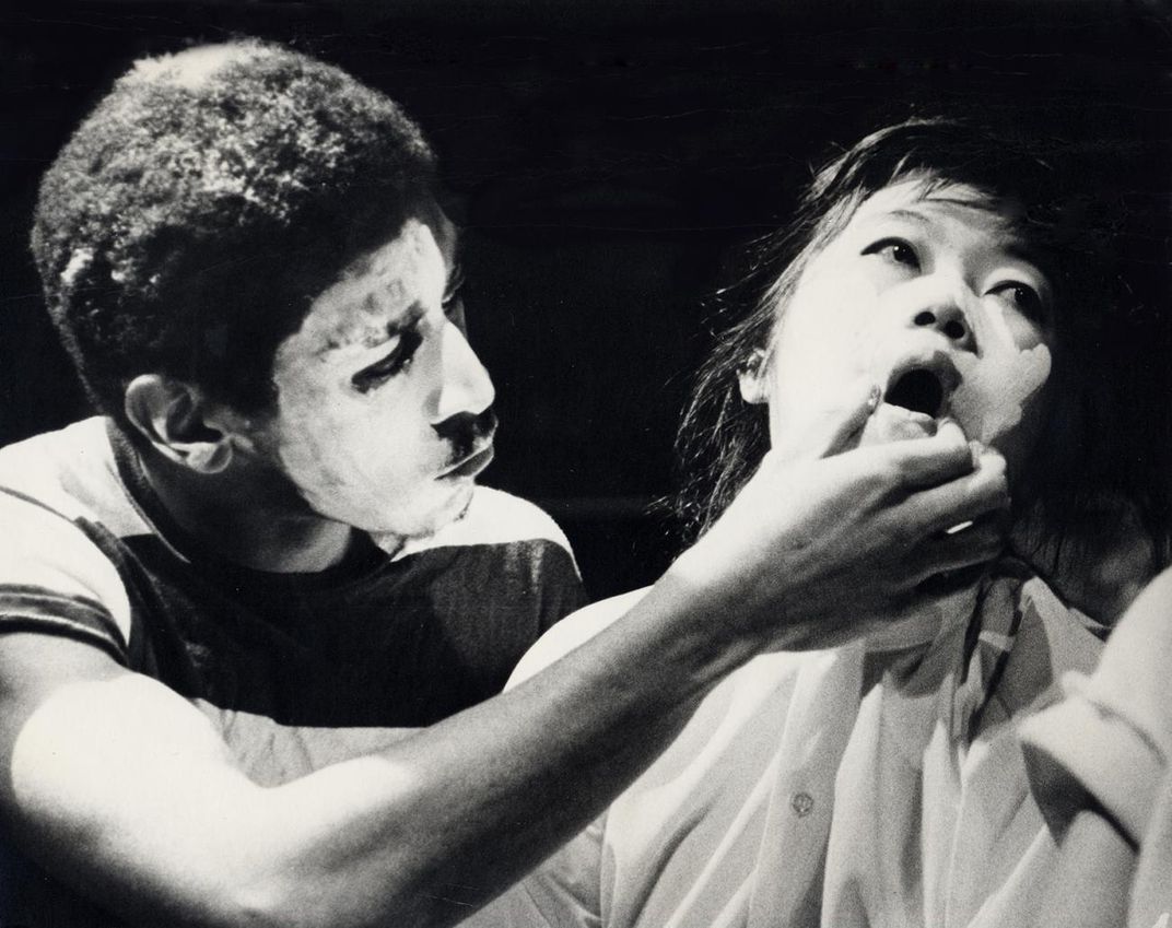 A film still of a man holding a woman's mouth. 